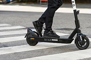 a man crossing a city street using an electric scooter