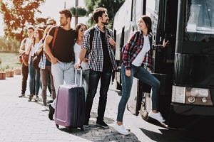 happy travelers standing in queue holding luggage waiting their turn to enter bus