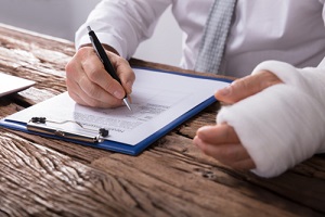 businessperson with broken arm filling health insurance claim form on wooden desk