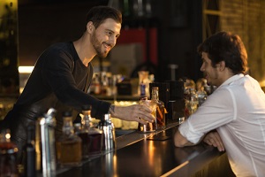 male bearded bartender smiling giving his client a drink while working at the bar communication friendly positivity entertainment leisure occupation job luxury lifestyle club weekend service