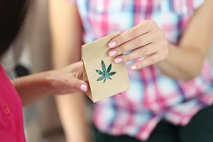 woman handing over small bag with a marijuana leaf imprint on the side