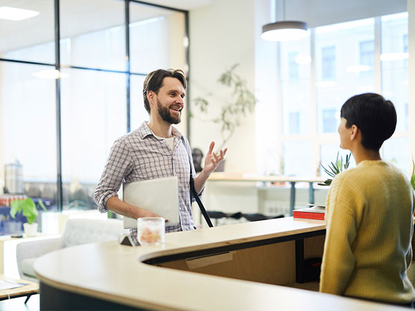 man holding laptop talking with hotel receptionist