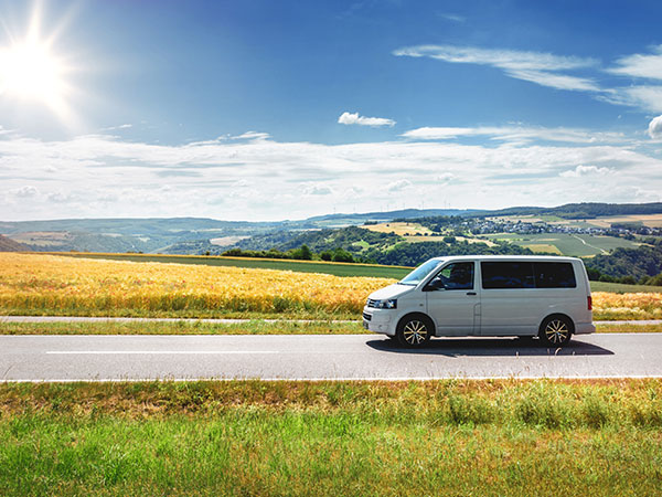 white van driving by road with crops