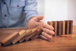 close up of businessman hand stopping wooden block from falling in the line of domino