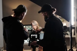 back view of two young men standing in front of camer aand using steadicam while shooting new commercial with female model