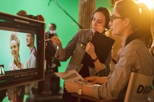 female director in chair looks at display talks with assistant