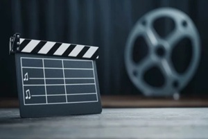 film clapperboard on wooden surface, background featuring a film reel