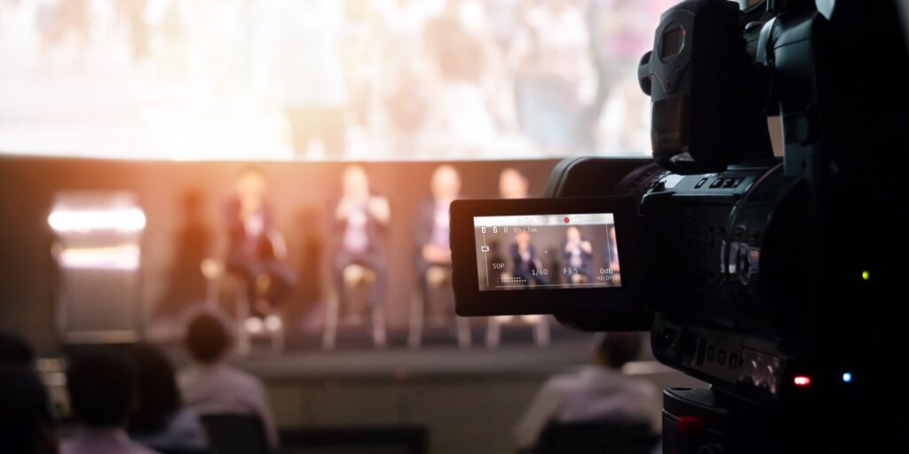Professional video camera filming a live commercial production shoot with crew and stage lighting in the background