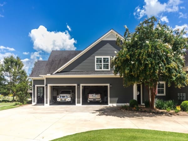 Front of a large home with cars in the garages.